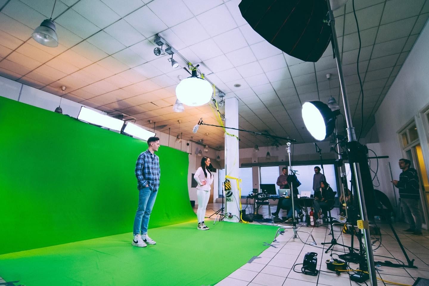 Presenters and crew in a temporary green-screen studio with cameras and lighting.